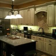 Warm beige kitchen with dark granite island, pendant lights, and cream cabinets under recessed lighting