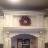 White fireplace mantel with crown molding and a red holiday wreath above an arched opening