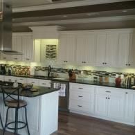 Bright white kitchen with island, dark countertops, bar stools, and under-cabinet lighting