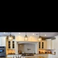 Bright white kitchen with island, pendant lights, built-in ovens, and a large central range hood