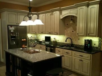 Warm kitchen with cream cabinets, black granite island, pendant lights, and stainless-steel appliances.