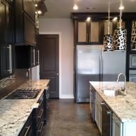 Modern kitchen with dark cabinets, granite counters, stainless steel appliances, and a central island with pendant lights