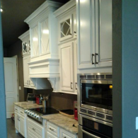 Modern white kitchen with cabinets, stove, range hood, and built-in stainless steel ovens