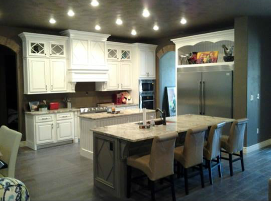 Modern kitchen with white cabinets, island seating, stainless fridge, and dark walls