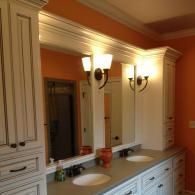 Bathroom vanity with white cabinets, double sinks, and wall sconces against orange walls.