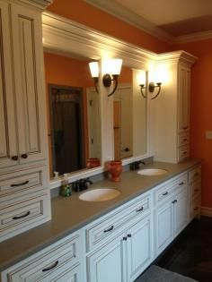White bathroom vanity with double mirrors, sconces, and orange walls by a sink counter