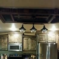 Kitchen with wood cabinets, stainless steel fridge, microwave, and hanging pendant lights under a dark ceiling.