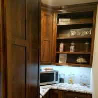 Wooden kitchen cabinet with open shelves, microwave, and a sign reading “He is good”