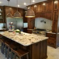 Modern kitchen with dark wood cabinets, granite island, and stainless steel refrigerator and range hood