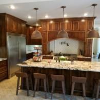 Modern kitchen with dark wood cabinets, granite island, pendant lights, and stainless steel appliances.