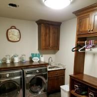 Laundry room with front-loading washer and dryer, wood cabinets, countertop sink, and hanging clothes rack