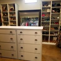 Walk-in closet with white drawers, built-in shelves of shoes and hats, and a mirrored alcove.