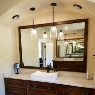 Bathroom vanity with large mirror, white sink, pendant lights, and wooden cabinets