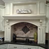 White kitchen cabinetry framing a stove and tiled backsplash, with a “Watson” sign above the range.