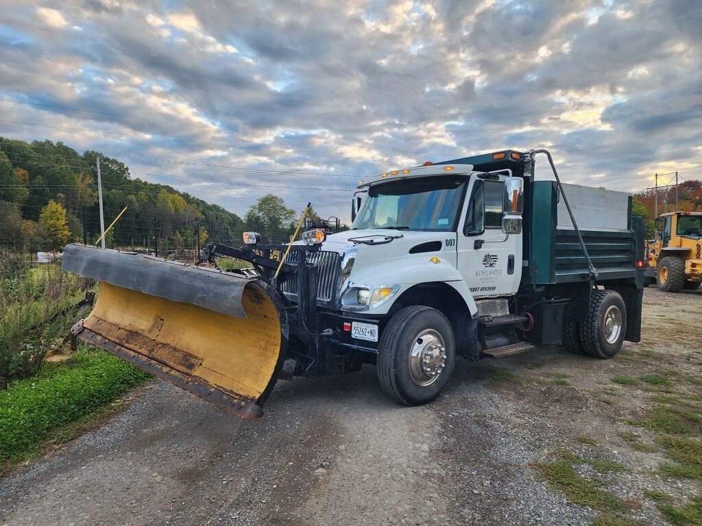 A dump truck with a snow plow attached to it is parked on the side of a dirt road.
