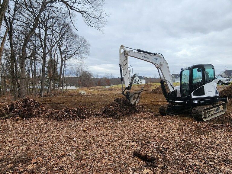 A white excavator is digging a hole in a field.
