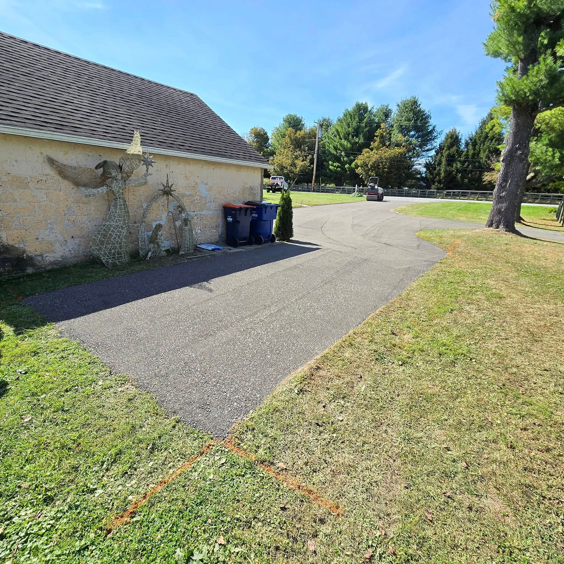 A driveway leading to a house with trash cans on the side of it.