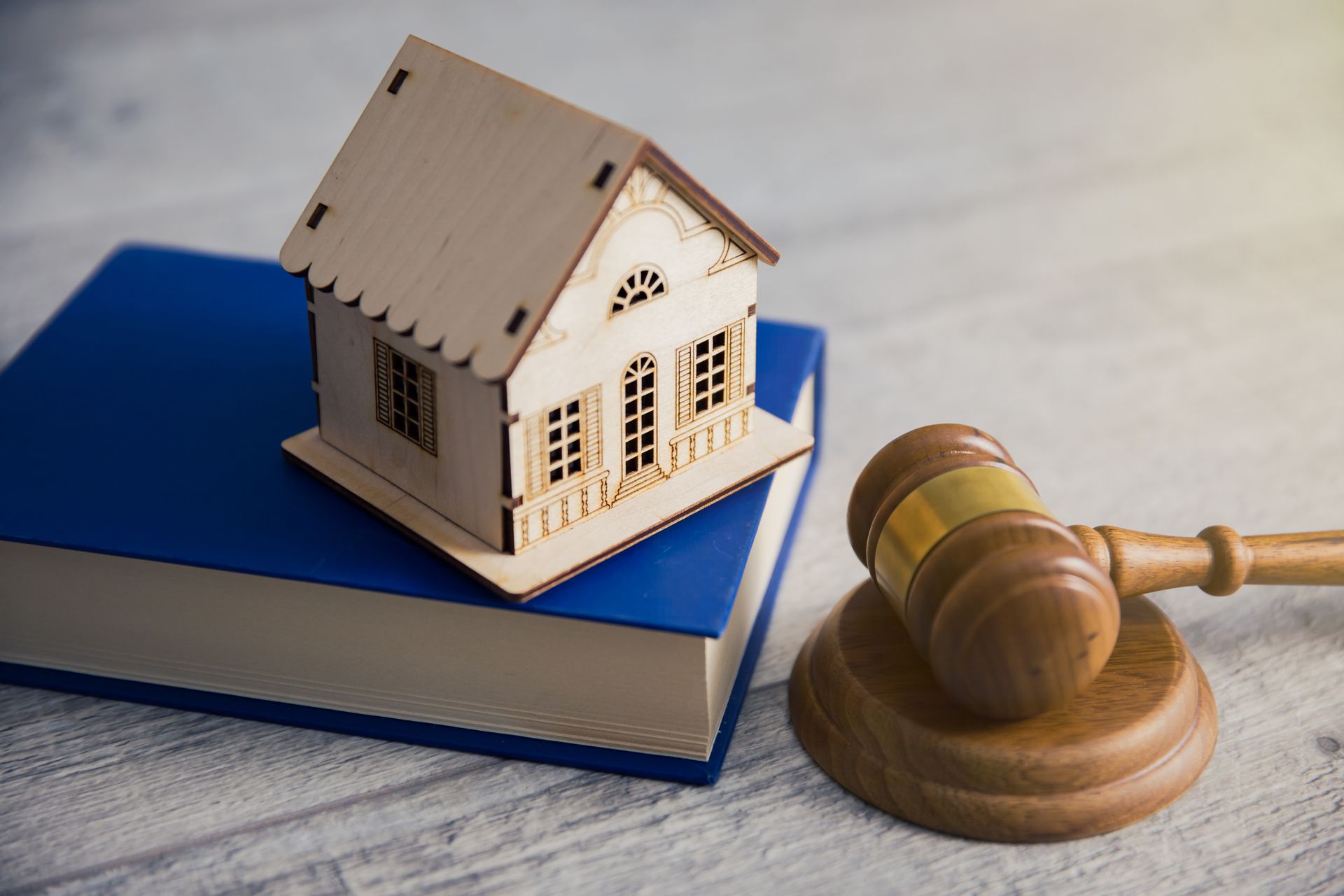 Wooden house model on a book, next to a gavel. Legal concept.