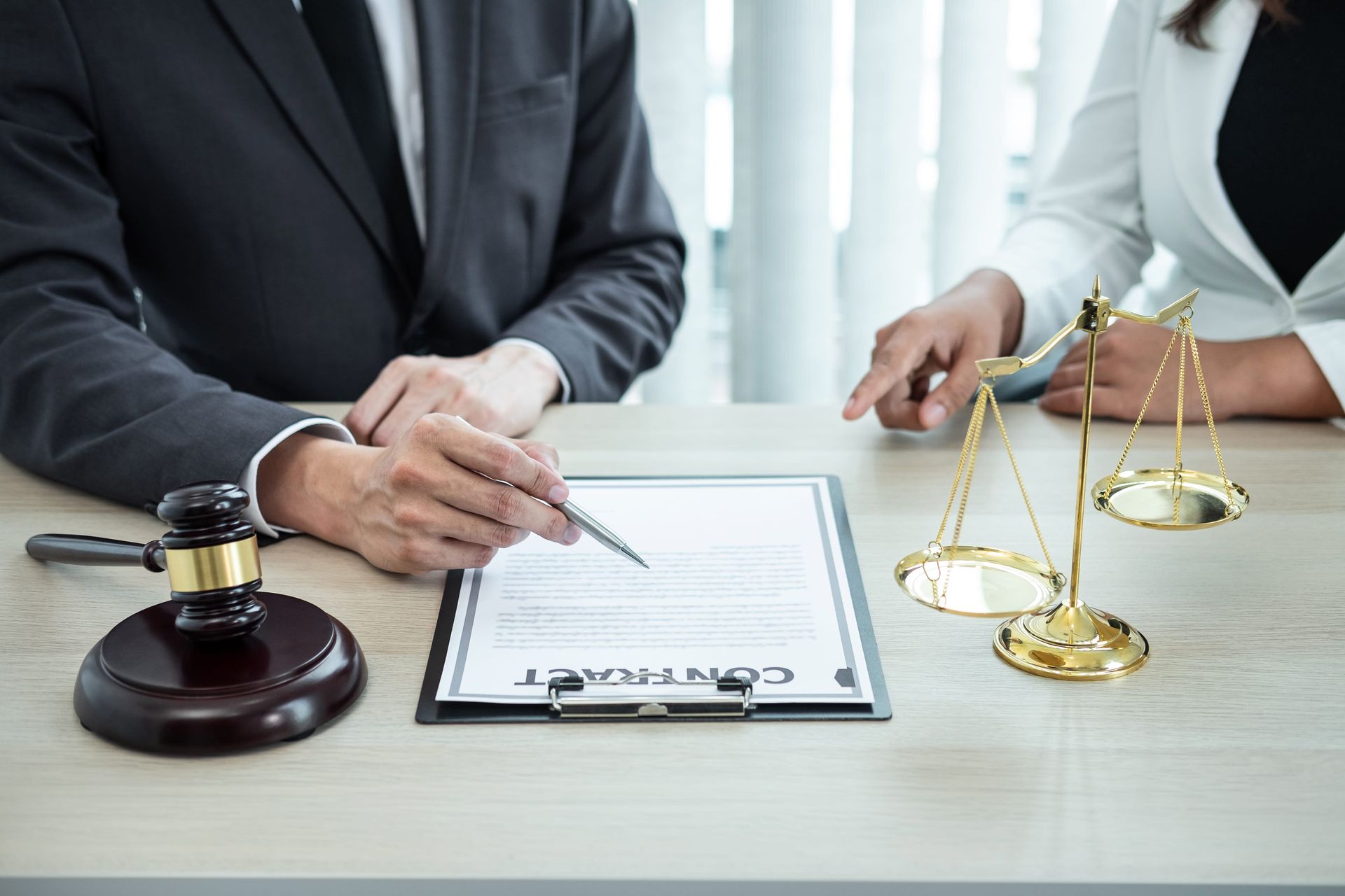 Lawyer pointing to a contract beside a gavel and scales of justice on a desk