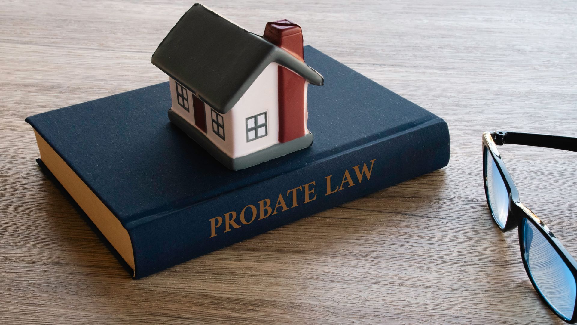 Model house on a blue book labeled “Probate Law,” with eyeglasses on a wooden table.