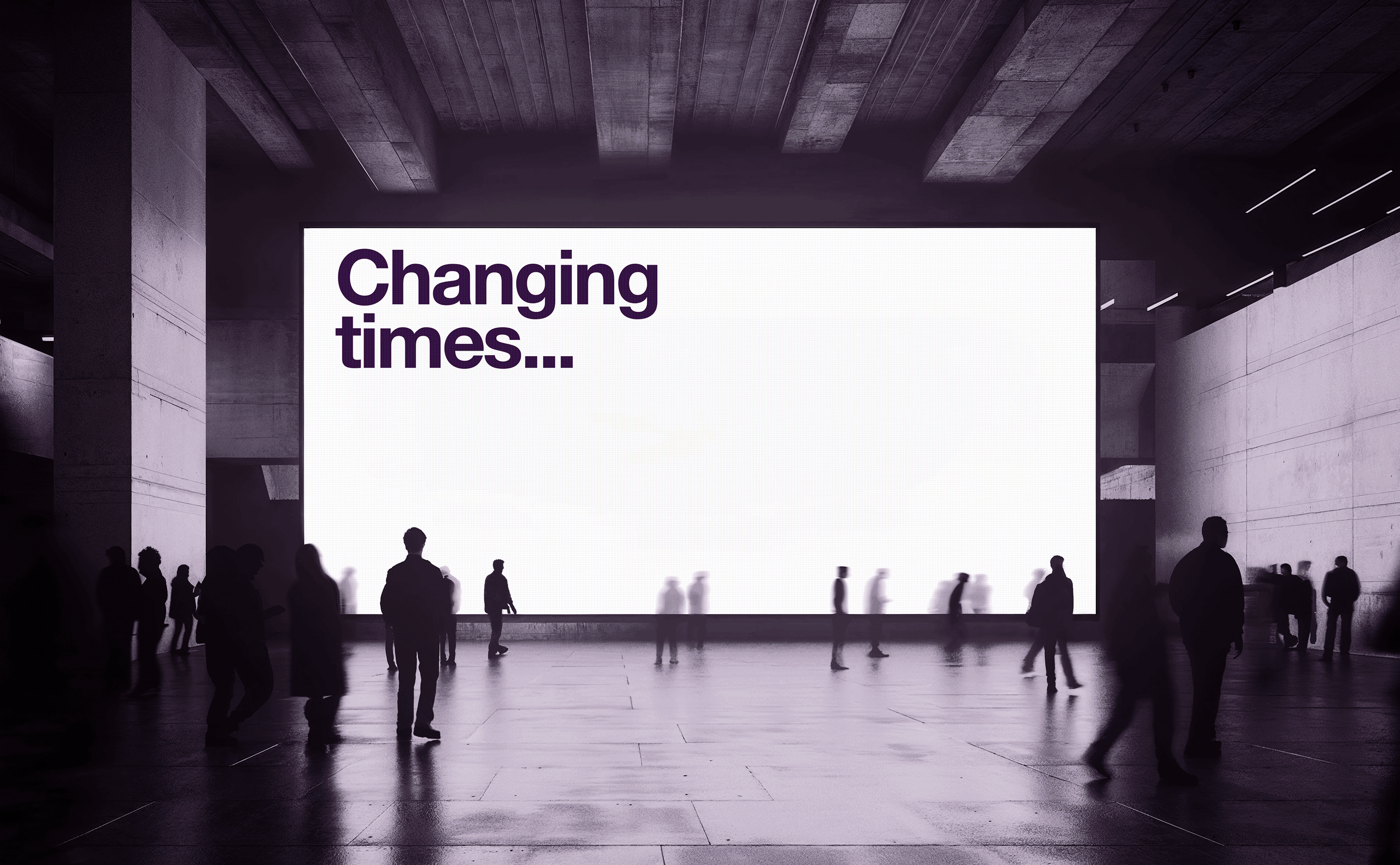 People walk in a large, modern space, in front of a bright screen with the words 