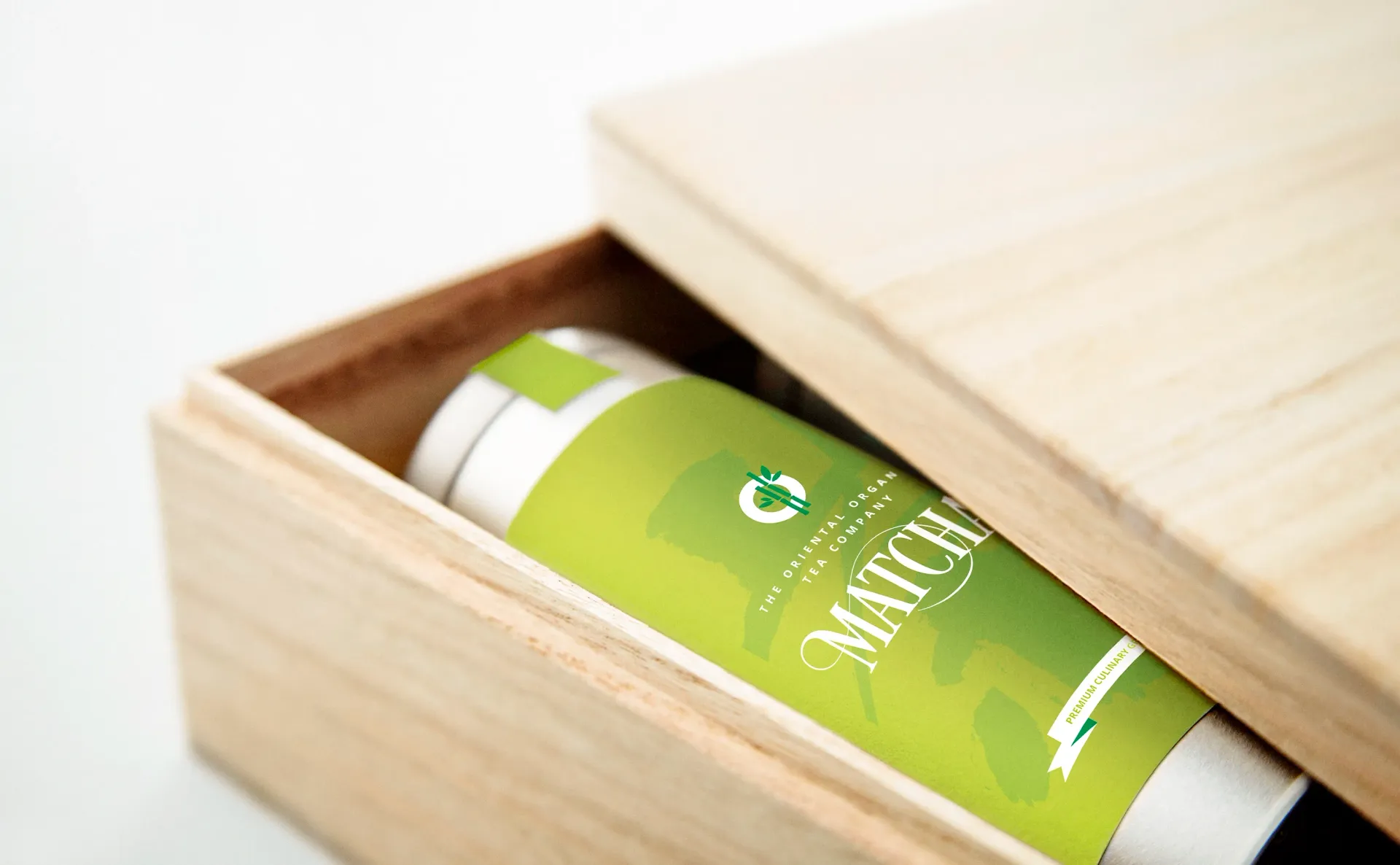 Matcha container in a wooden box, with a green and white label and slightly open lid.