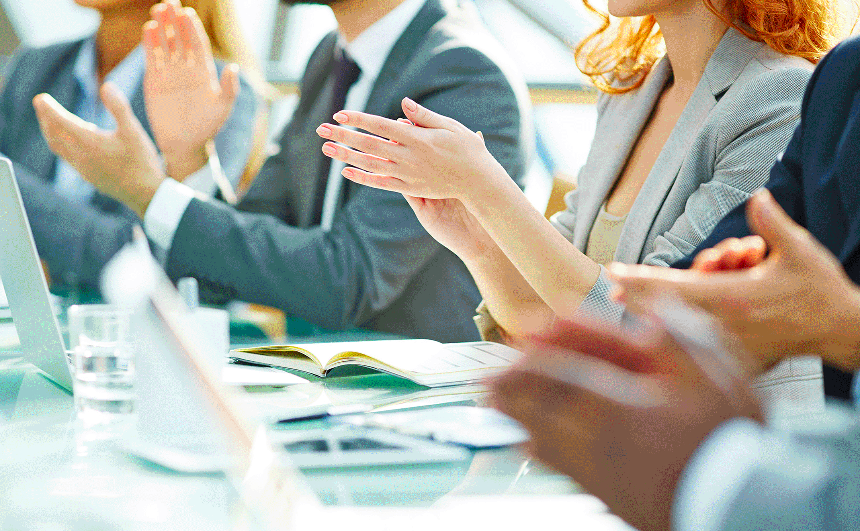 People in business attire clapping at a meeting table.