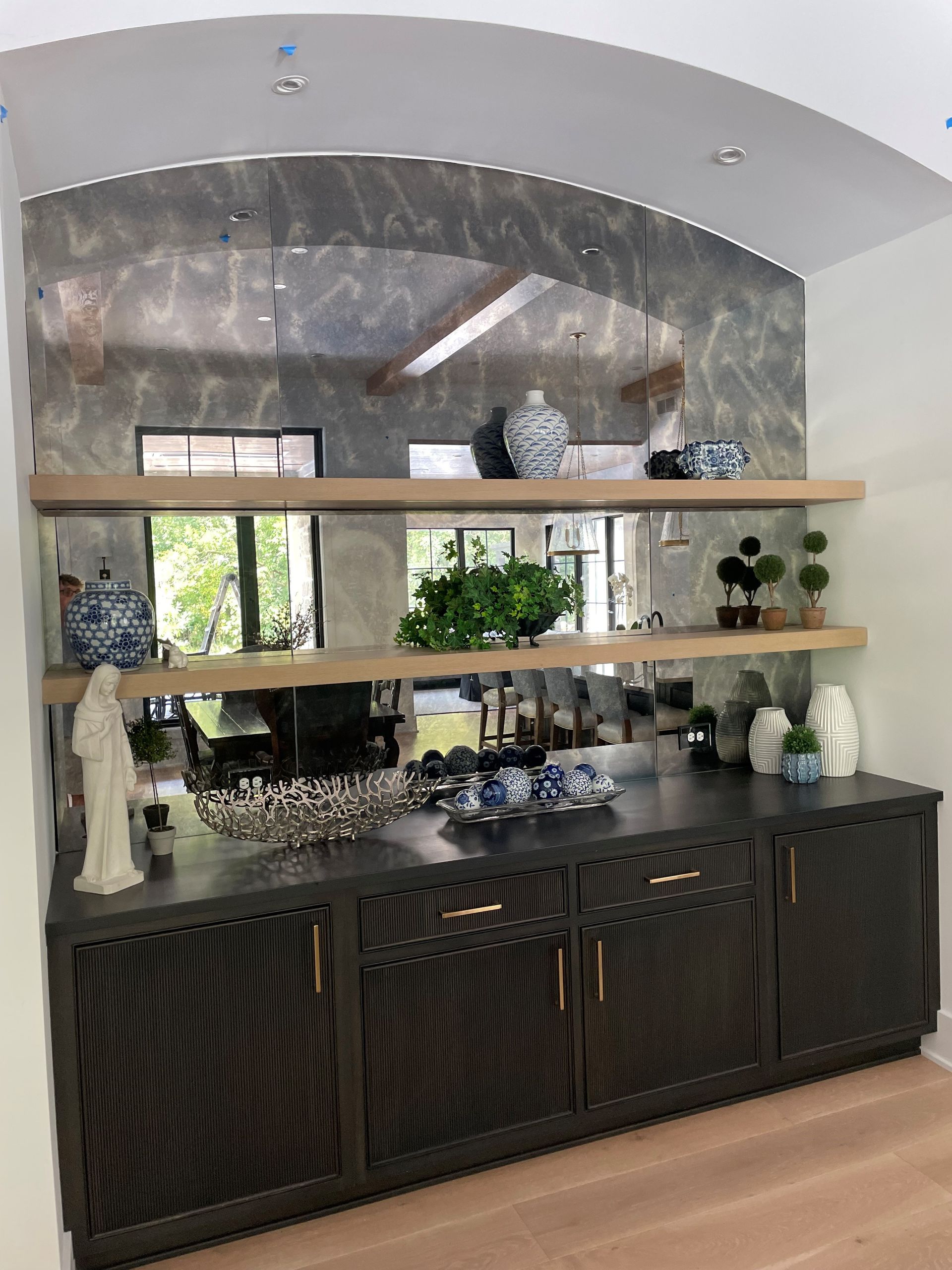 Built-in dark bar with gold hardware, mirrored backsplash, wooden shelves with plants and decor.