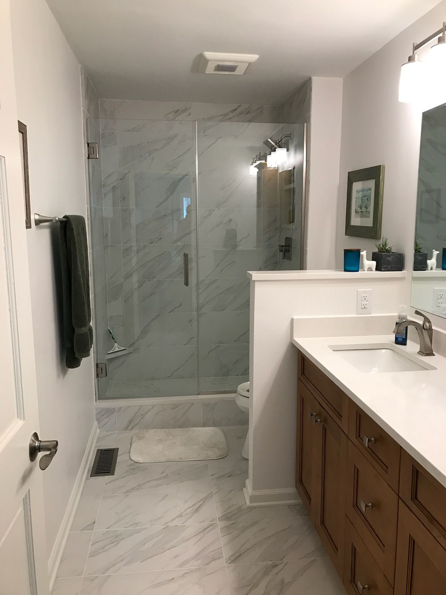 Bathroom with glass shower, white walls, wood vanity, and marble-look floor.