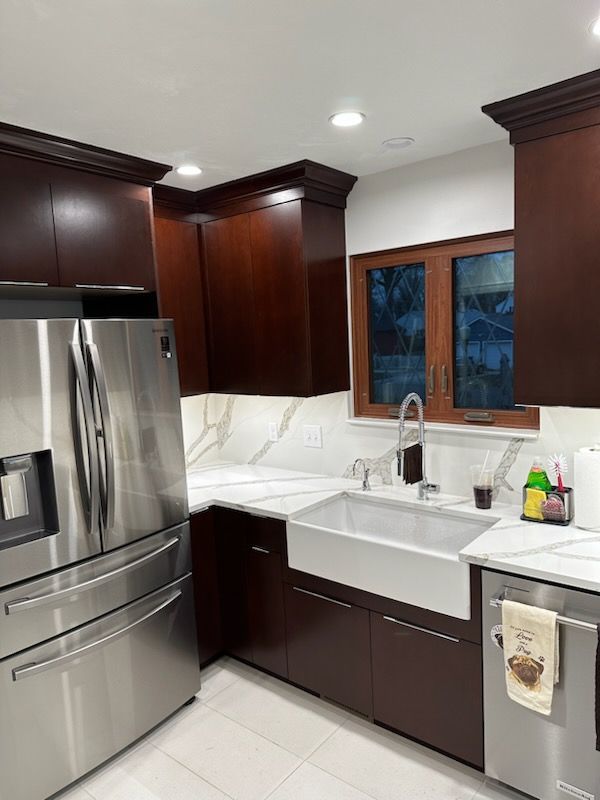 Modern kitchen with dark wood cabinets, stainless steel appliances, and white countertops.