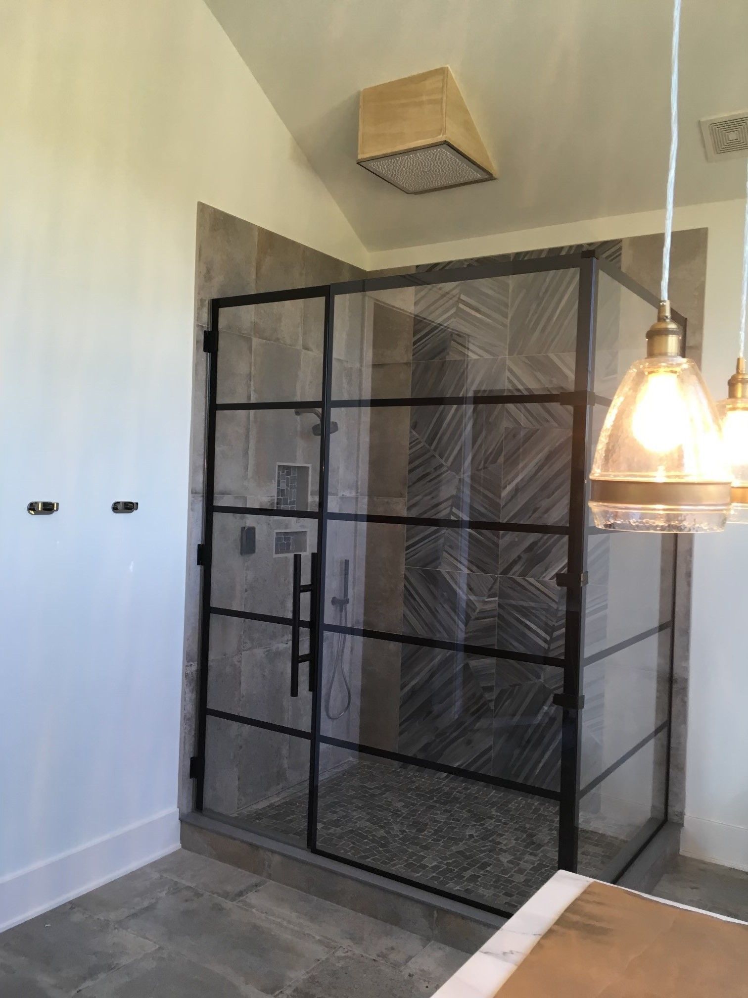 Shower with black framed glass doors, rain shower head, and pendant lights.