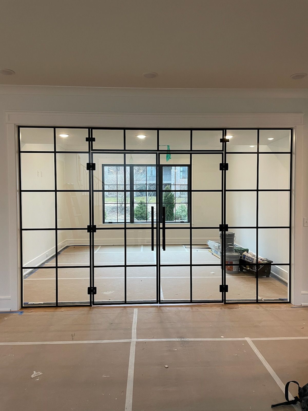Black-framed glass doors with grid design, leading to a room with interior windows.