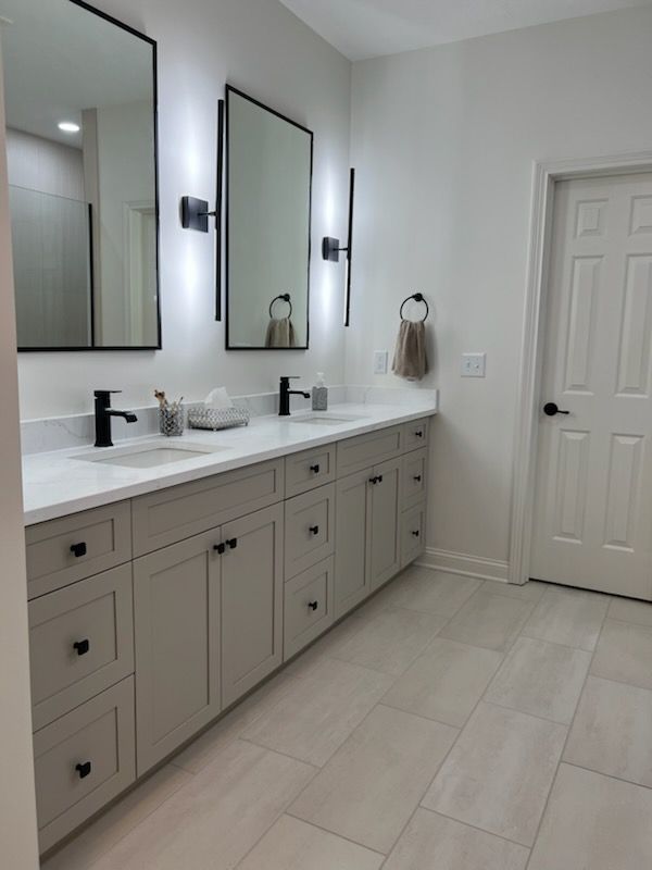 A modern bathroom featuring a grey double vanity, two rectangular mirrors with wall sconces, and light-toned tile flooring.