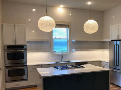 Modern kitchen with white and dark blue cabinets, double oven, and pendant lights.