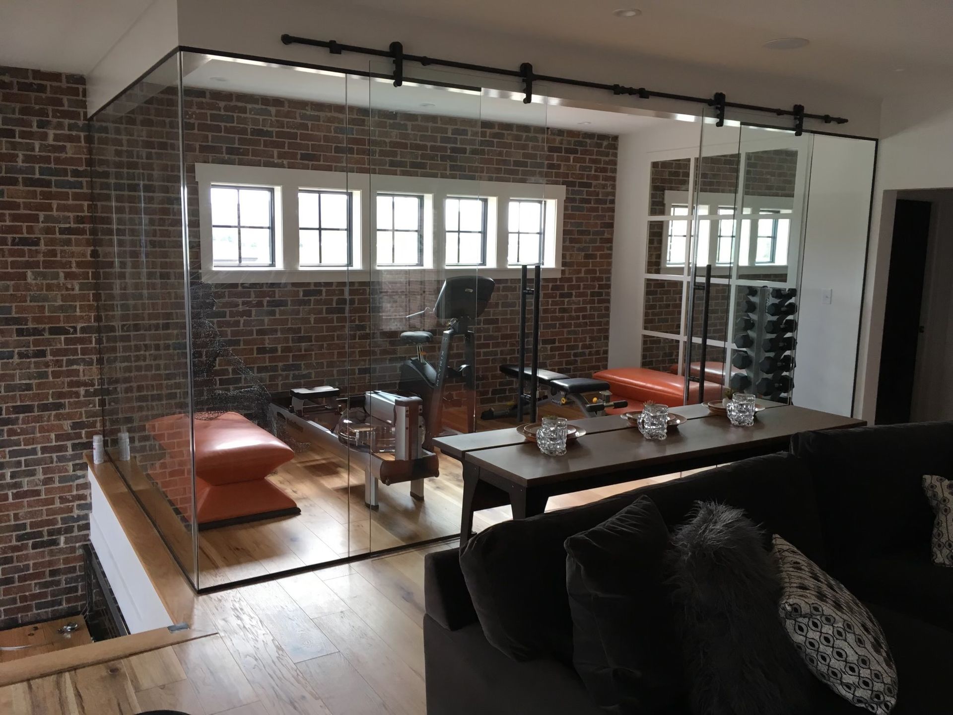 Glass-walled home gym with brick wall, exercise equipment, a bench, and a table visible through the glass.