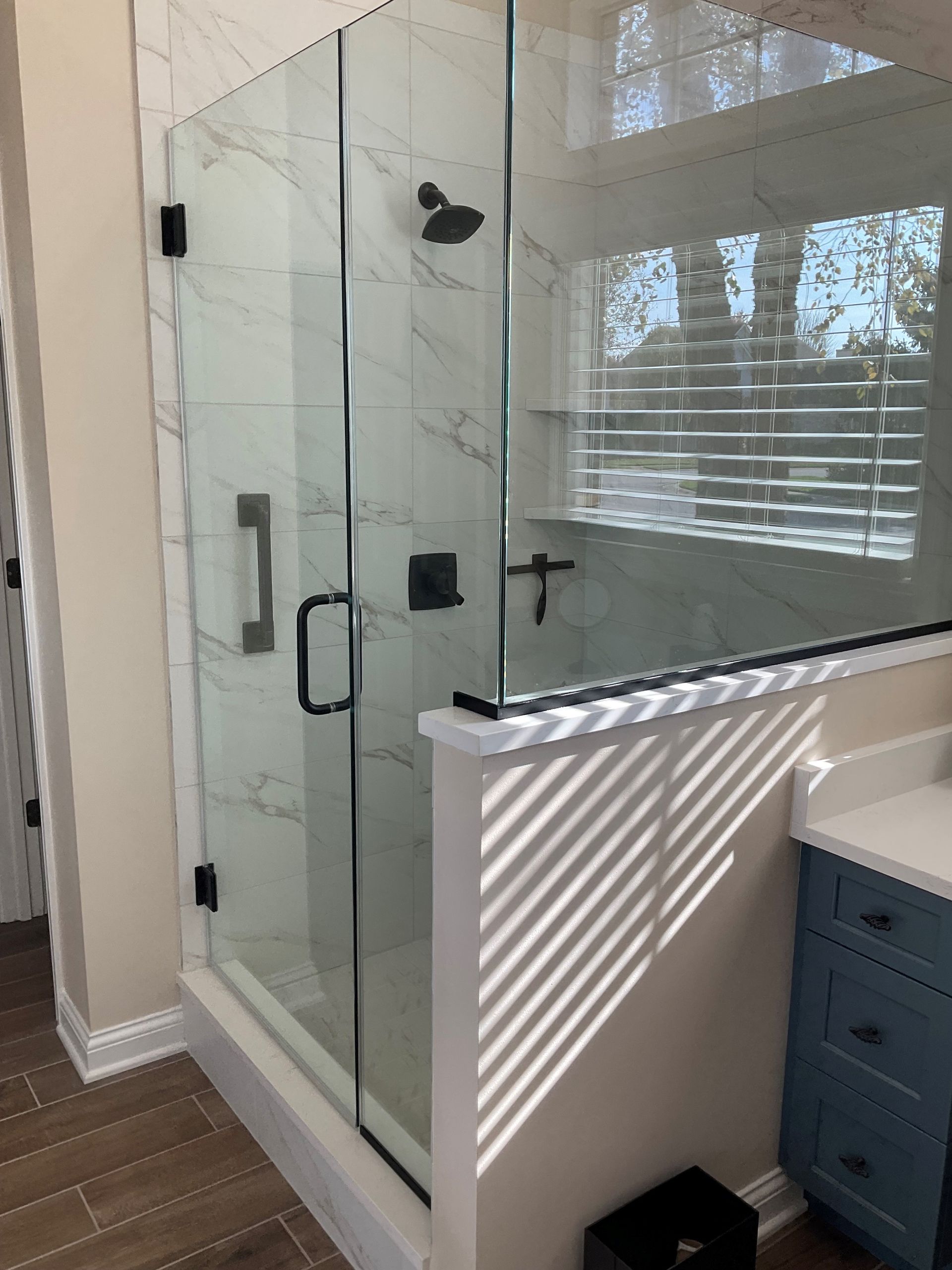 Glass shower enclosure with black fixtures and marble-look tile.