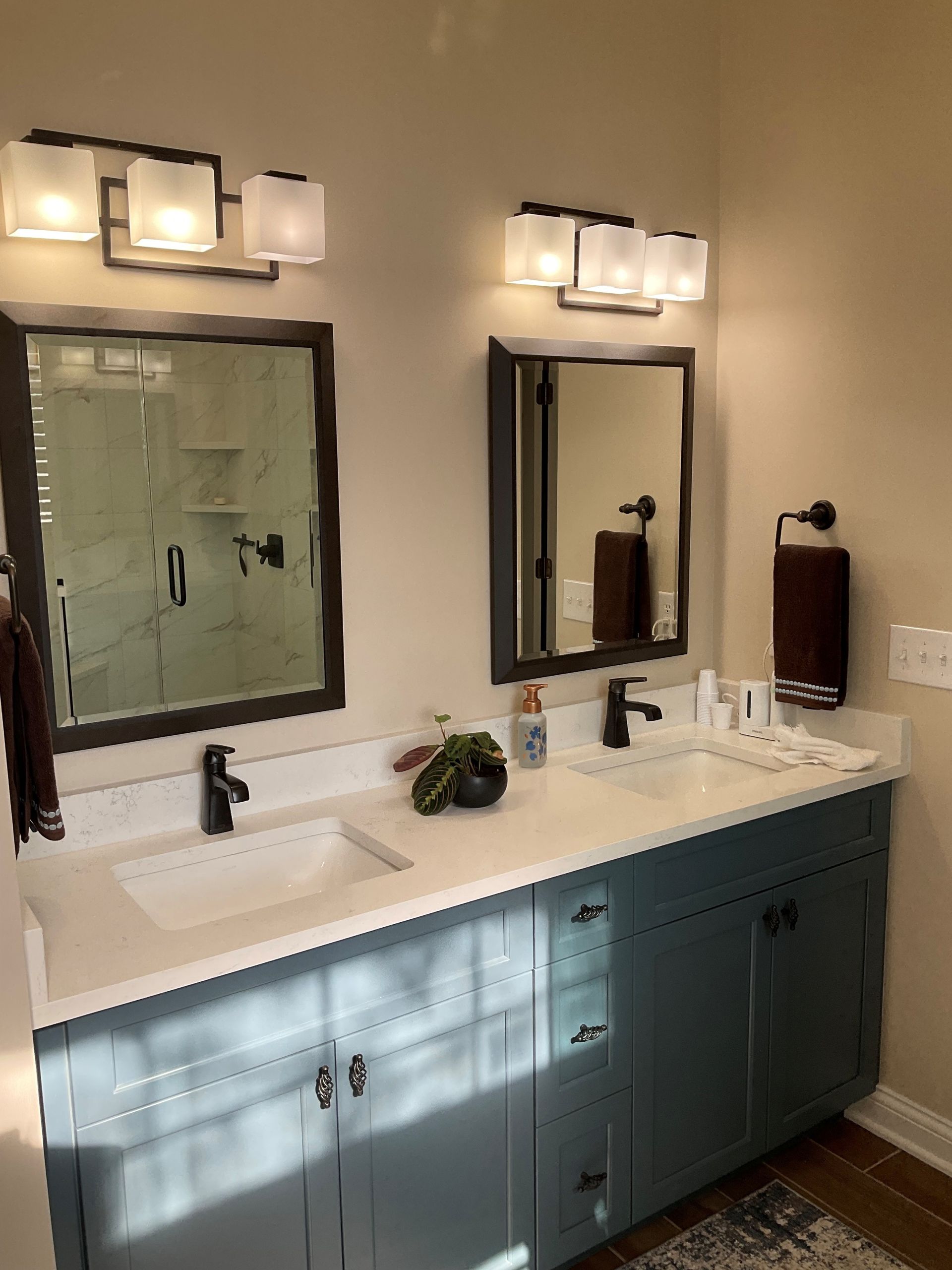 Bathroom with two sinks, blue vanity, white countertop, dark framed mirrors, and frosted glass light fixtures.