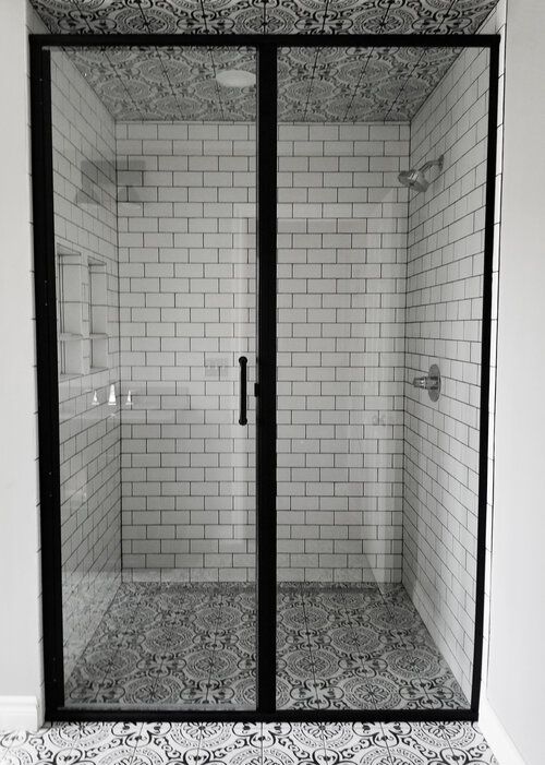 Shower with black frame, subway tile walls, patterned floor, and glass doors.
