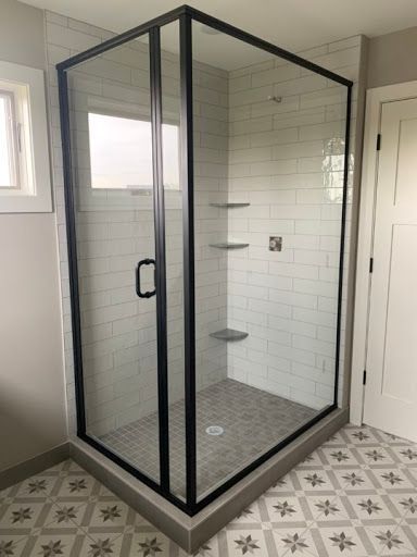 Black-framed glass shower enclosure in a bathroom with tiled walls and floor. Gray and white color scheme.