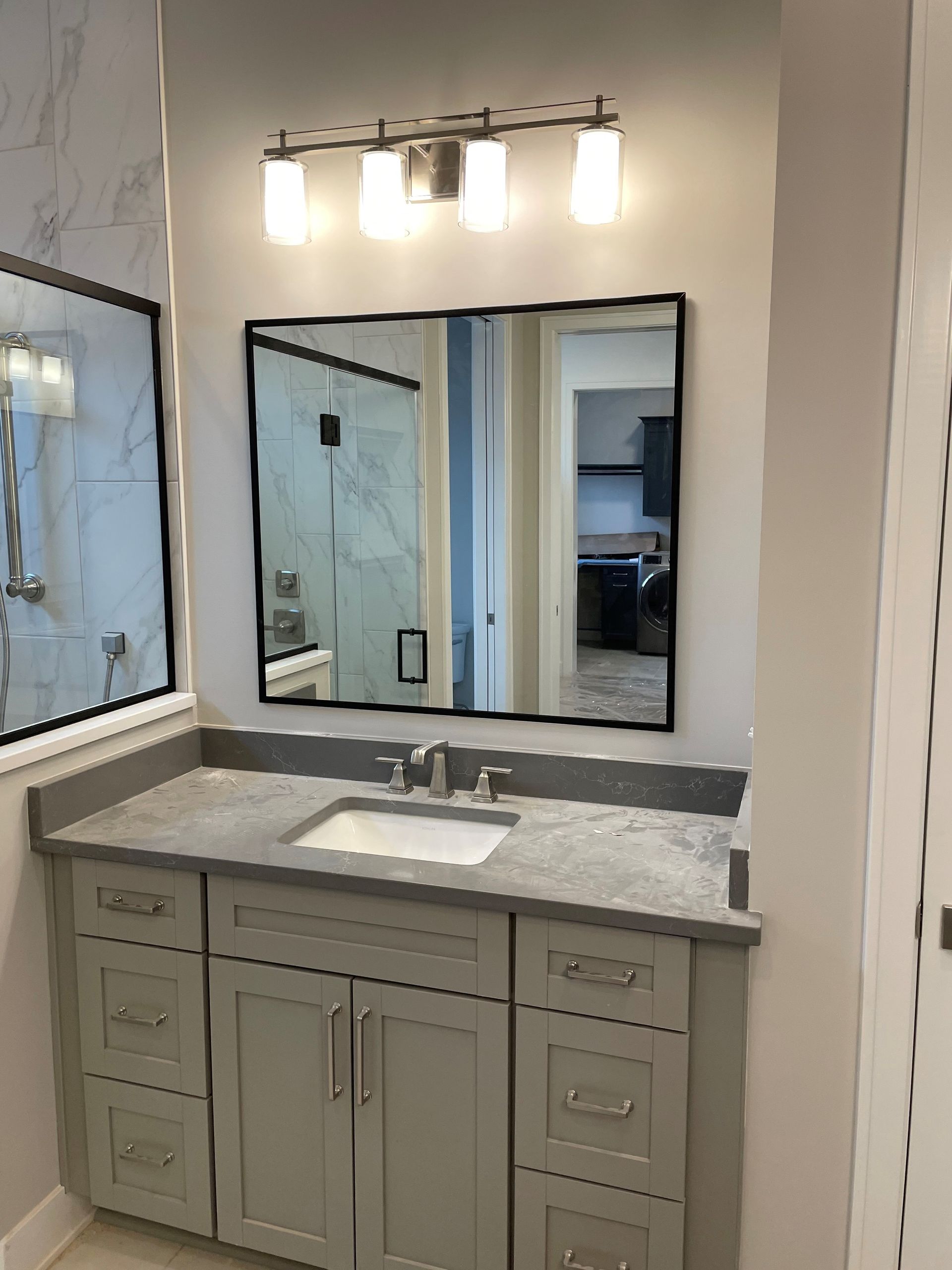 Bathroom vanity with gray cabinets, countertop, mirror, and a light fixture.