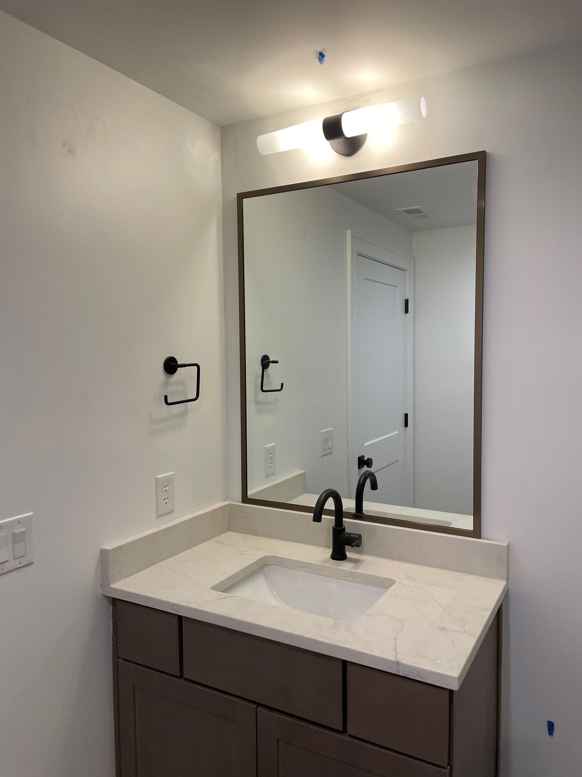 Bathroom vanity with a mirror, light, sink, and faucet. The cabinet is brown, walls are white.