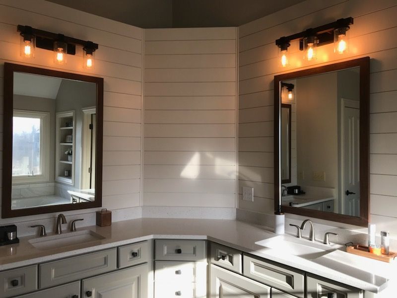 Bathroom with two mirrors, light fixtures, and white shiplap walls. Gray cabinets and white countertops.