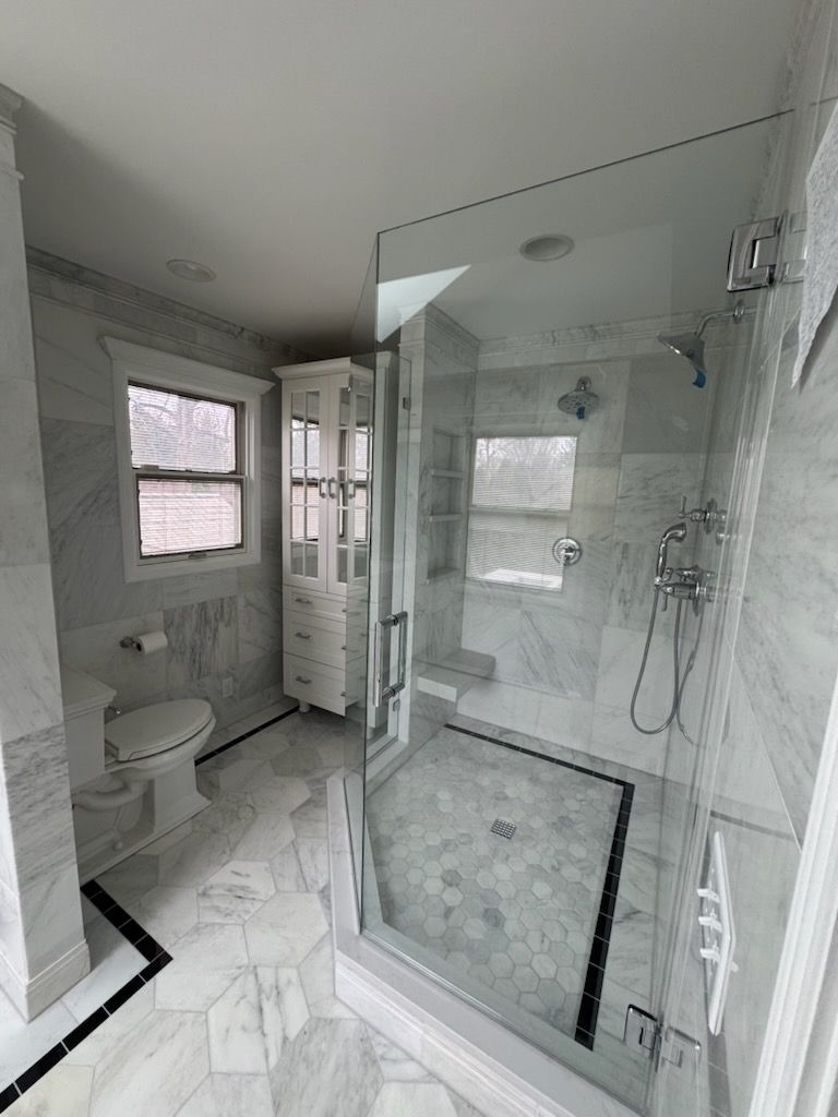 Luxurious marble bathroom with glass shower, white cabinetry, and hexagon floor tile.