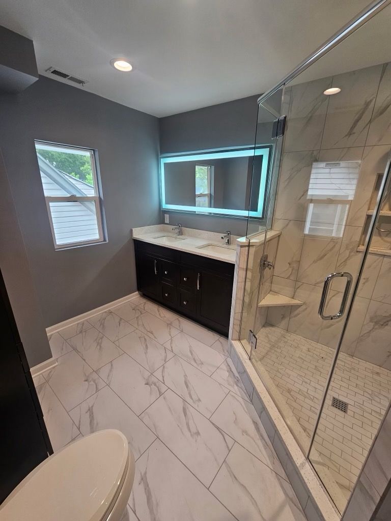 Modern bathroom with gray walls, marble tile floors, double vanity, and glass shower.