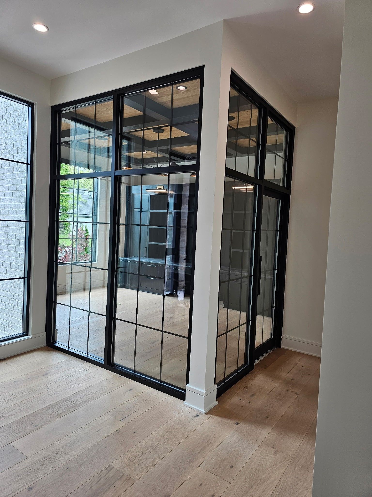 Black-framed glass partition wall with grid design. Light wood floor, white walls, and recessed lighting.