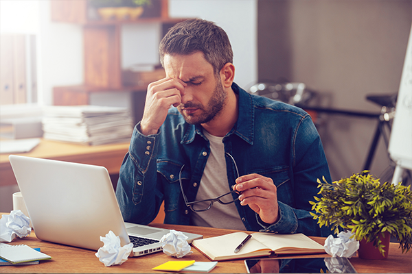 a man is sitting at a desk with a laptop and rubbing his forehead .