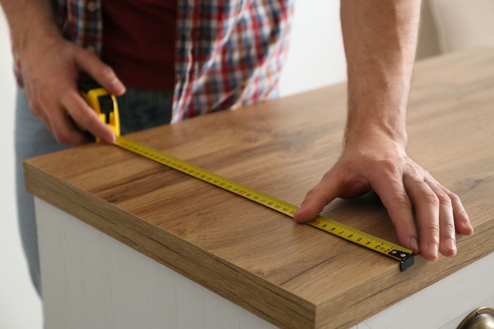 Person measuring a wooden board with a tape measure on a workbench