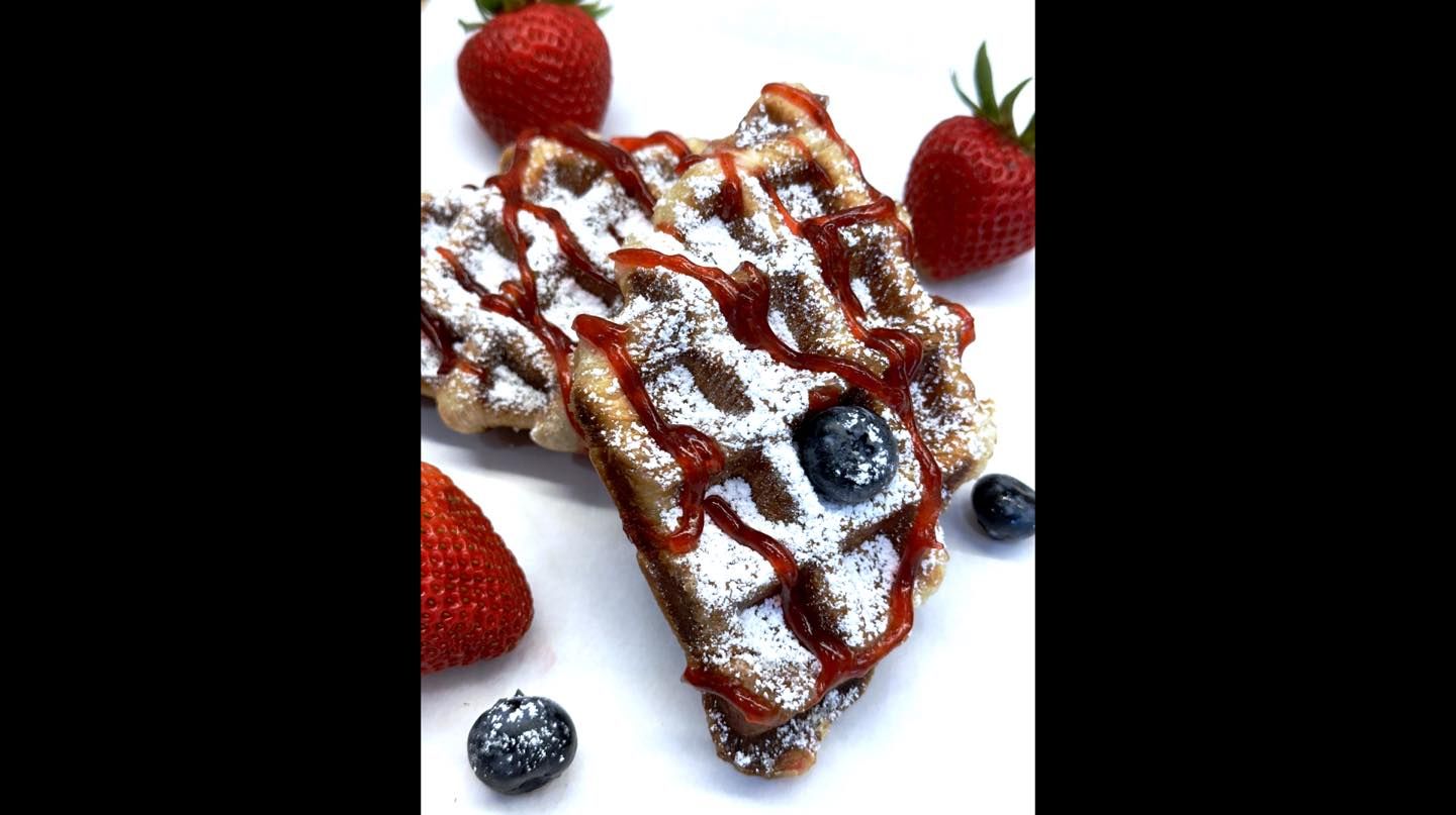 A waffle with strawberries and blueberries on top of it.