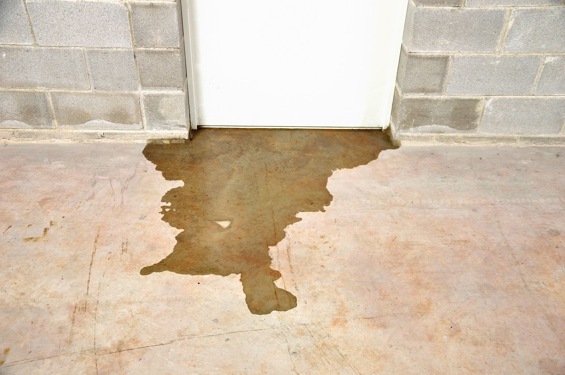 Water-stained concrete floor below a white door in a cinderblock wall