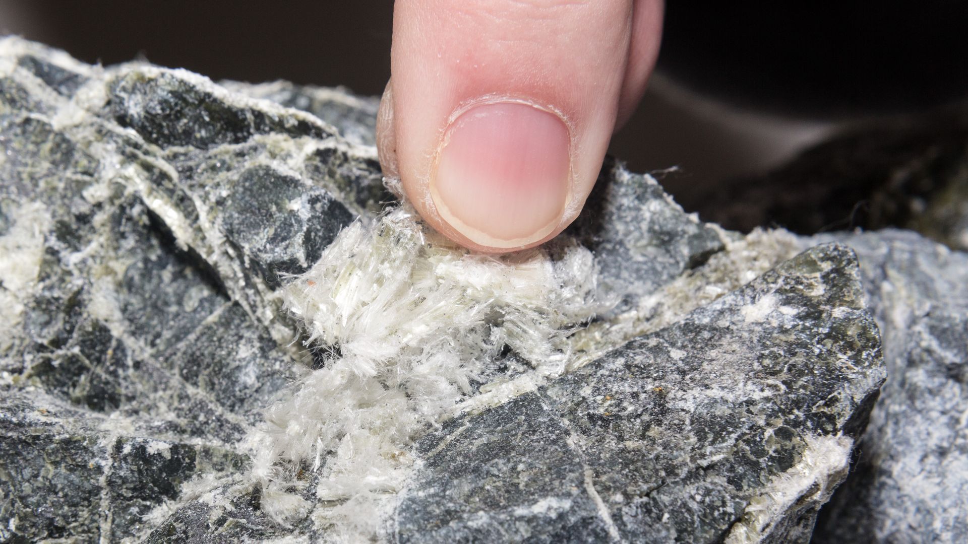 Close-up of a finger pointing at a white vein in a gray rock surface